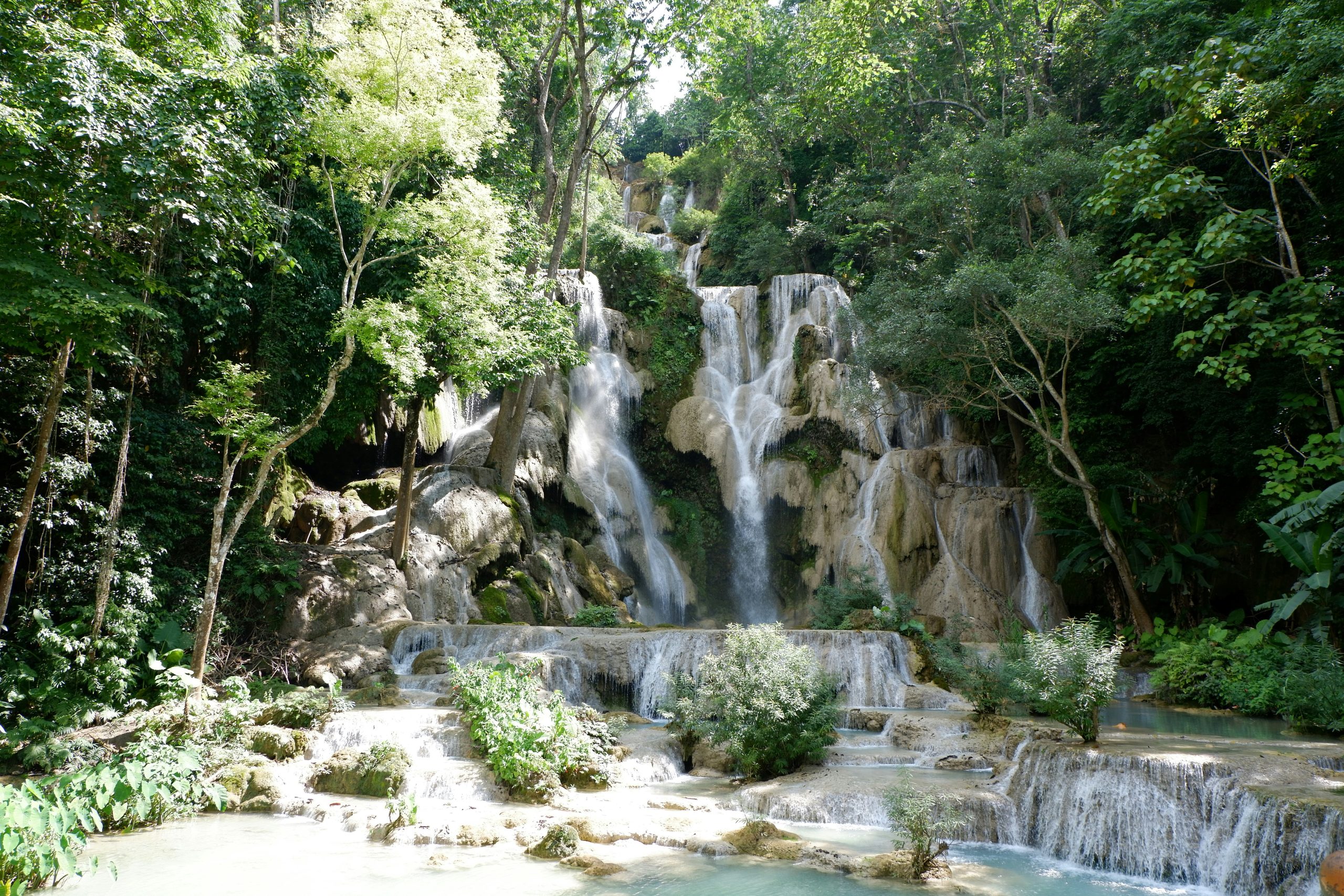 Turquoise waterfall surrounded by lush jungle in Laos